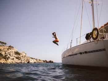 Full length side view of man jumping from catamaran into sea against sky