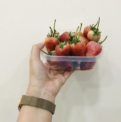 Close-up of hand holding strawberry over white background