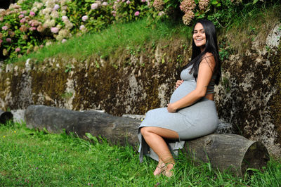 Young pregnant brazilian woman touching her belly, sitting on wood log in the summer garden person