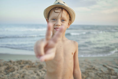 Smiling boy showing peace gesture while standing at beach