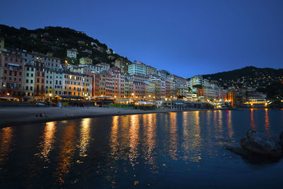 Illuminated buildings by lake against sky at dusk