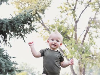 A small boy walks joyfully through the park with trees in the background