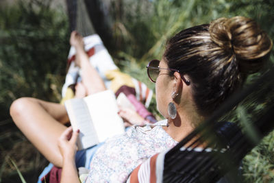 Woman with sunglasses reading a book lying on a hammock.