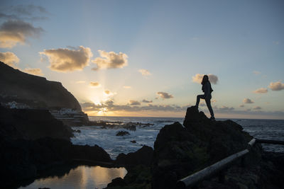 Man standing on rock by sea against sky during sunset