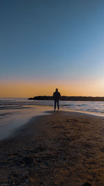 Silhouette person standing on beach against sky during sunset