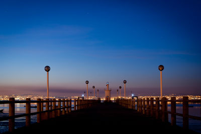 Street lights on pier by sea against blue sky