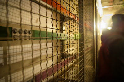 Close-up of man seen through metal fence against wall