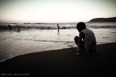 Silhouette people sitting on beach against clear sky