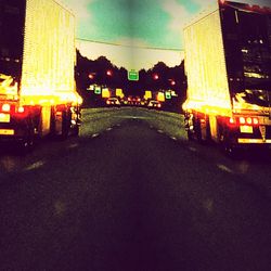 Illuminated road by buildings against sky at night