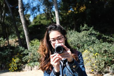Portrait of young woman photographing against trees