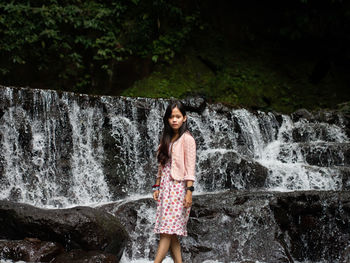 Young woman in pink dress standing against waterfall