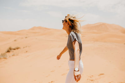 Side view of young woman standing on sand dune