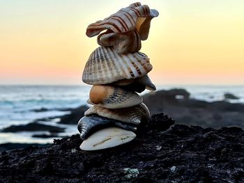 Stack of pebbles on rock at beach against sky during sunset