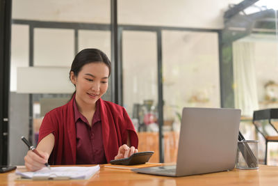 Young woman using phone while sitting on table