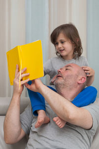 Father and son together enjoying reading and discussing school homework from yellow textbook.