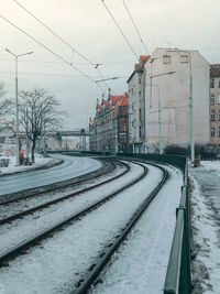 Snow covered railroad tracks in city against sky