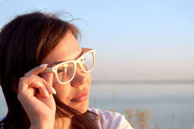 Close-up portrait of young woman holding eyeglasses against sea