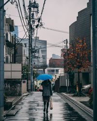 Rear view of man walking on wet street during rainy season