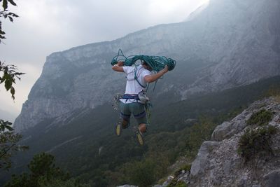 Rear view of man jumping with rope against mountain range