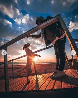 Man standing on railing against sky during sunset