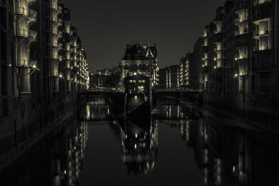 Bridge over canal amidst buildings in city at night