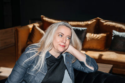 Pensive woman with platinum blonde hair relaxing in a denim jacket indoors
