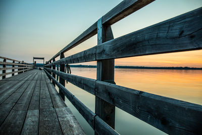 Pier over river against sky during sunset