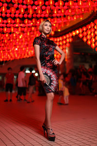 Full length portrait of young woman standing against red wall