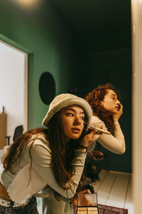 Young female friends applying make-up at home