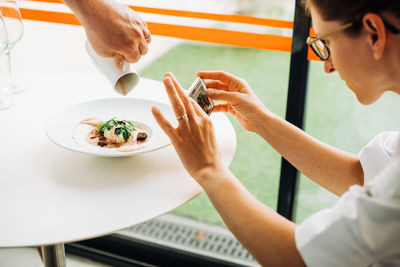 Woman taking photos of food with smartphone while waiter serving meal