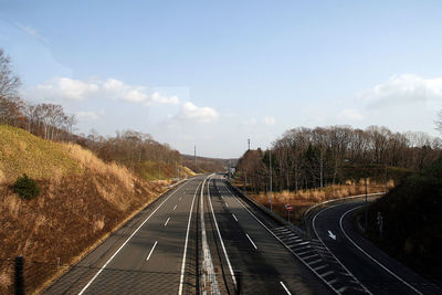 Empty road along trees and plants against sky