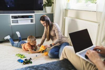 Mother and son playing with toy by father working on sofa at home