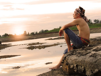 Woman on rocks at shore against sky during sunset