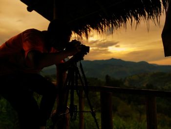 Silhouette man photographing against sky during sunset