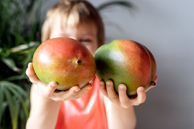 A little boy holding mango fruit in his hands.