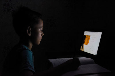 Side view portrait of boy holding camera in dark room