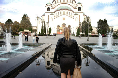 Rear view of woman standing by fountain in city