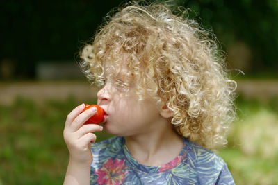 Boy with curly blond hair eating tomato at park