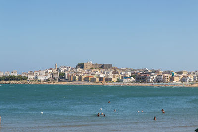 Buildings by sea against clear blue sky