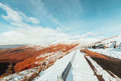 Snow covered road by mountain against sky