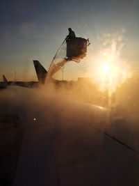 Silhouette man splashing water on aircraft wing from hydraulic platform at airport against sky