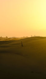 Rear view of man walking at beach against clear sky during sunset