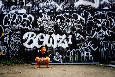 Man sitting by graffiti on wall