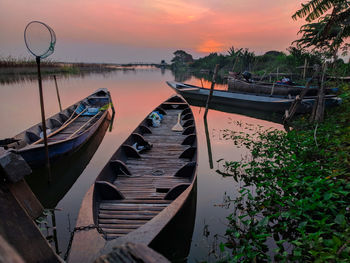 Boats moored in lake against sky during sunset