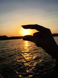 Silhouette hand by sea against sky during sunset