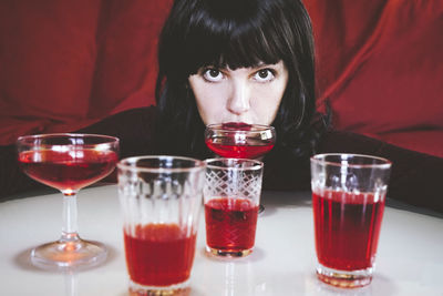 Woman drinking red alcohol drinks in various glasses on table