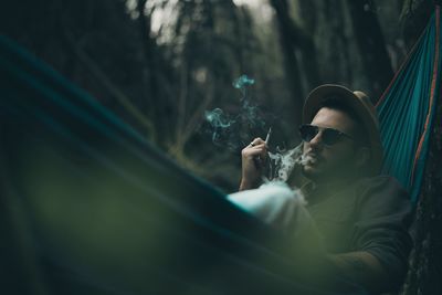 Man smoking cigarette while lying on hammock in forest