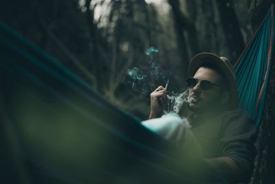 Man smoking cigarette while lying on hammock in forest