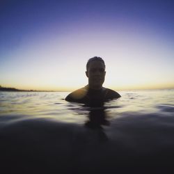 Portrait of young man swimming in sea against clear sky at sunrise