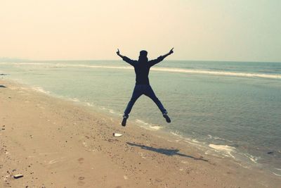 Rear view of man jumping at beach against sky